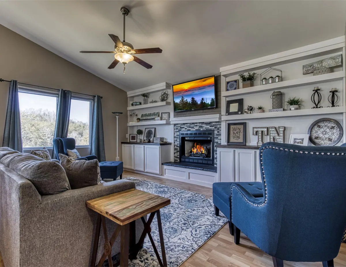 A cozy living room centered around a warm fireplace, with a plush blue armchair, a comfortable sofa, and shelves adorned with decor. The ambiance is intimate and inviting, ideal for unwinding after outdoor adventures.