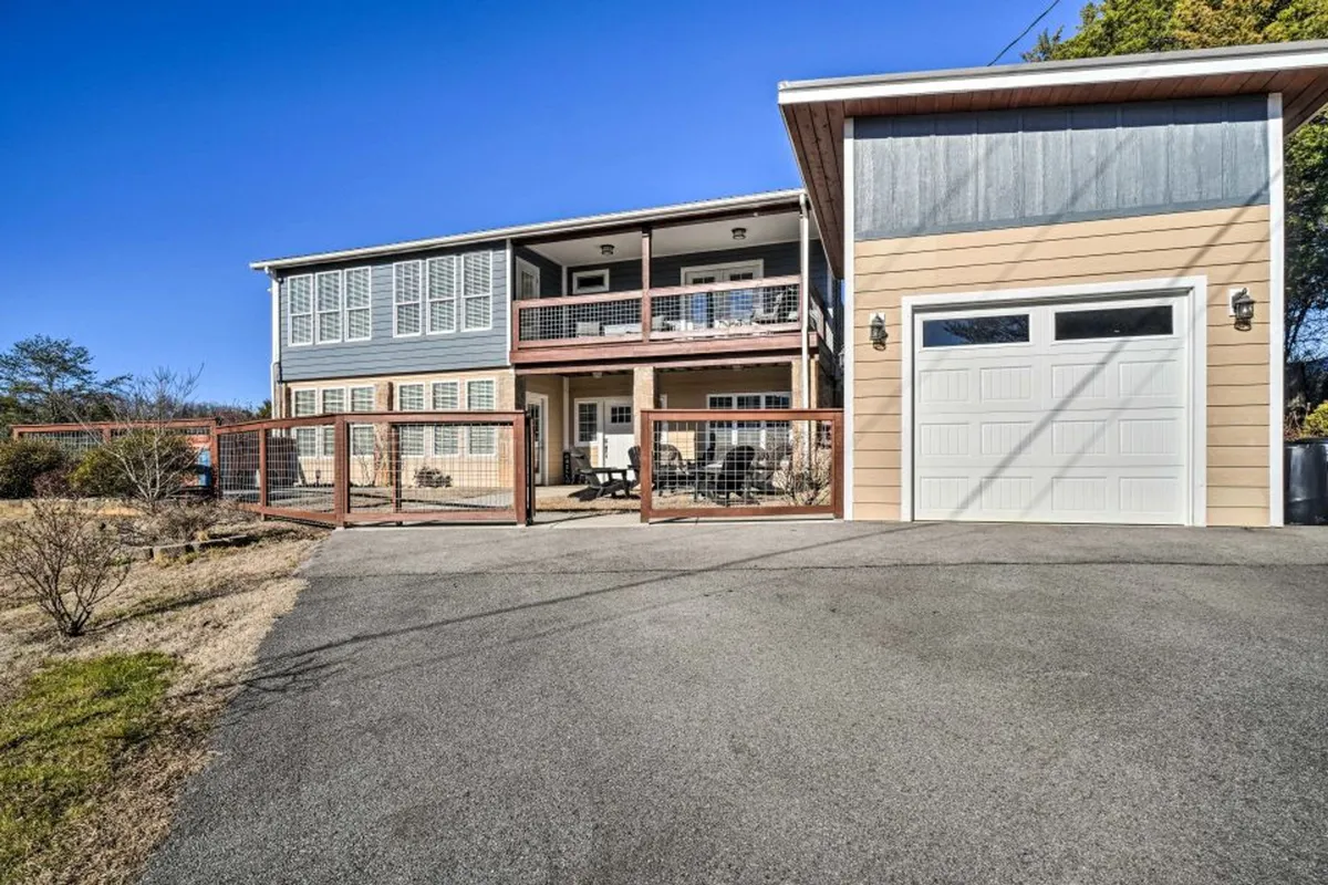 The image showcases a welcoming two-story modern house in Sevierville, Tennessee, with a spacious fenced yard, cozy front porch with sitting area, and garage. The scene exudes a warm, inviting atmosphere perfect for outdoor gatherings, family barbecues, and relaxing moments while enjoying sunset views or morning coffee as children play in the yard.