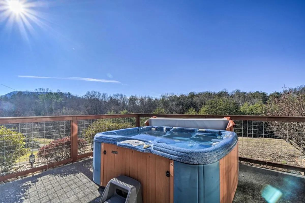 An inviting outdoor hot tub sits on a wooden deck, with sweeping mountain views in the background. The golden light of sunset bathes the scene, and the secure railing ensures privacy while guests relax and take in the scenery.
