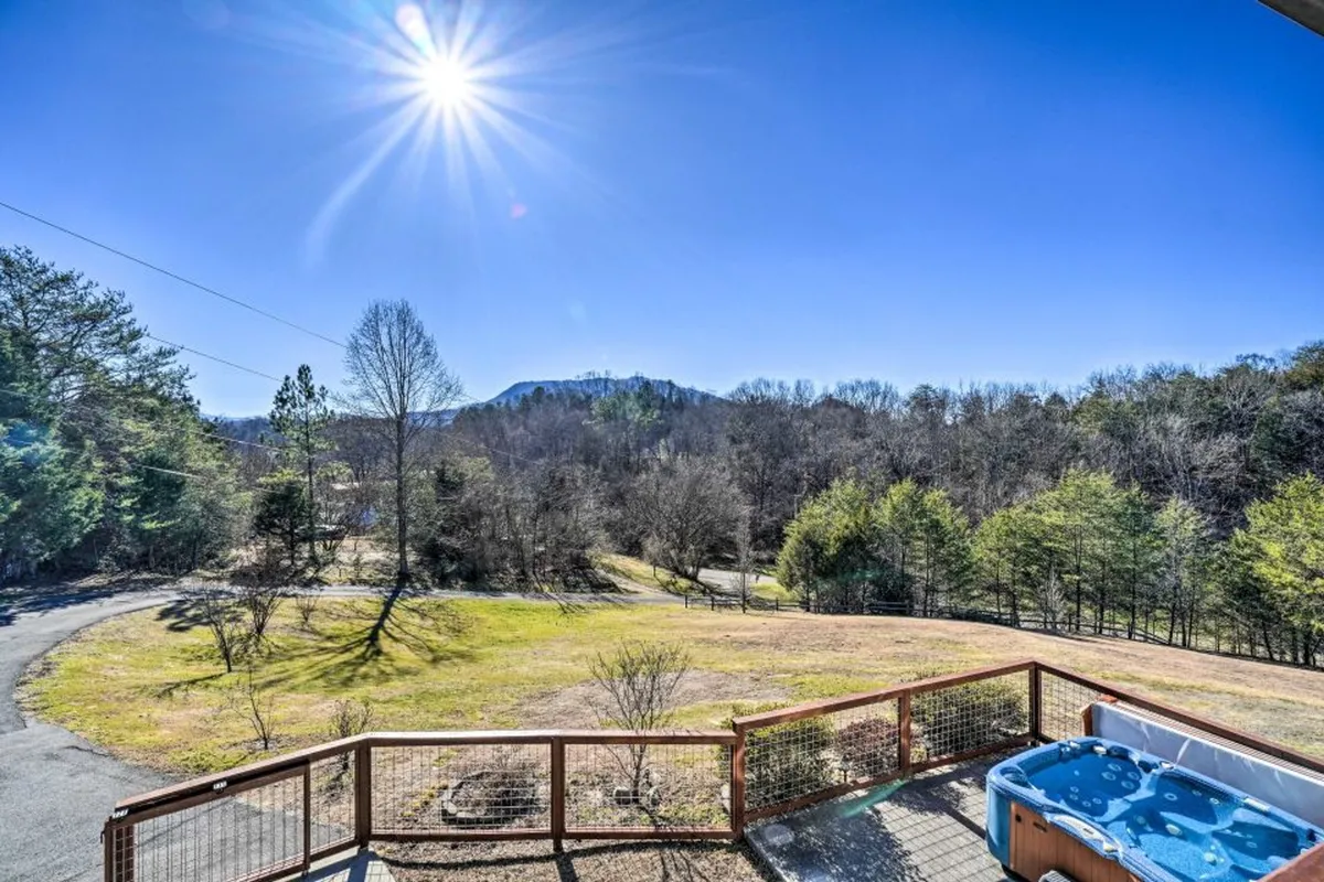This image features a stunning view of a mountain range framed by a hot tub on a wooden deck, set against a green landscape. The scene suggests relaxation after a day of adventure, with opportunities for enjoying nature walks, soaking in the hot tub, or stargazing at night.