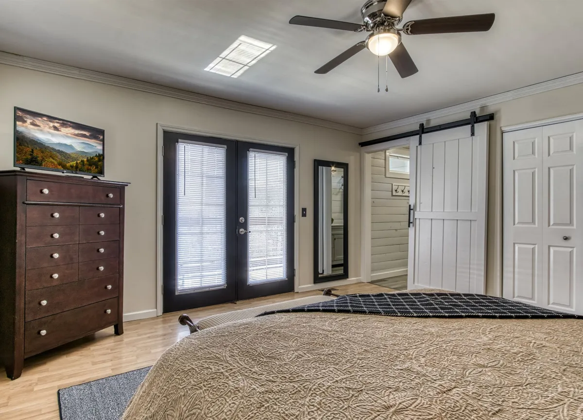 A serene bedroom with a comfortable bed, dresser, and sliding barn door offers a peaceful space bathed in natural light. The room is styled with soft, crisp linens and subtle mountain-inspired décor, evoking a cozy, restful retreat ideal for unwinding after a day of adventure.